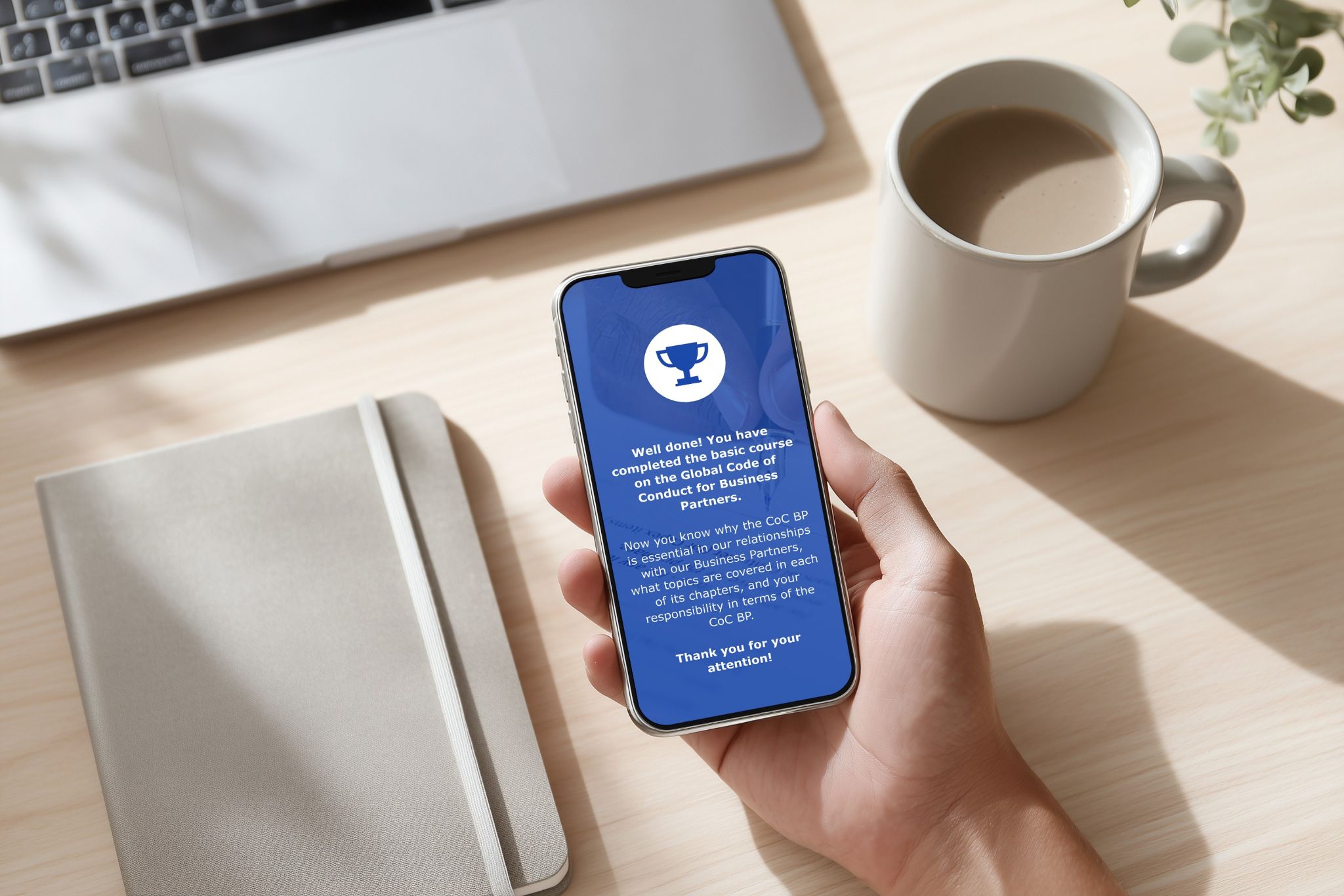 Person holding a smartphone displaying a completed Global Code of Business Conduct course.